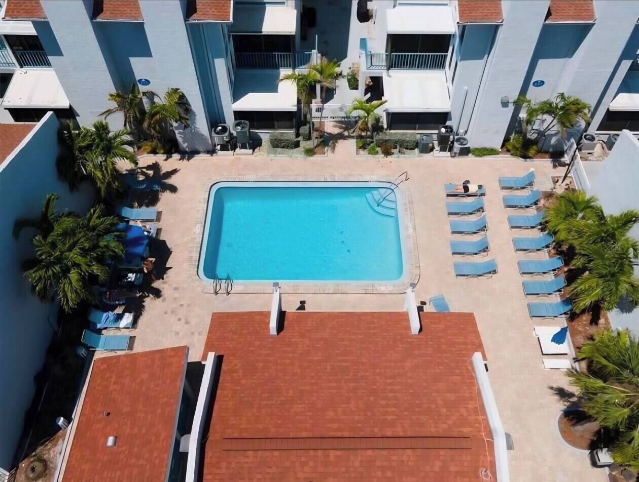 Ein Swimmingpool, umgeben von Liegestühlen und Palmen, mit einem Gebäude im Hintergrund.