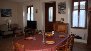 Ein Essbereich mit rotem Tischlein, Holzkstühlen, einem Fernseher und einer Tür mit Fenster.