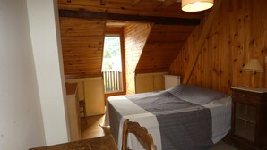 Ein Schlafzimmer im Dachgeschoss mit Holzboden, einem Bett, einem Nachttisch, einer Lampe und einem Fenster.