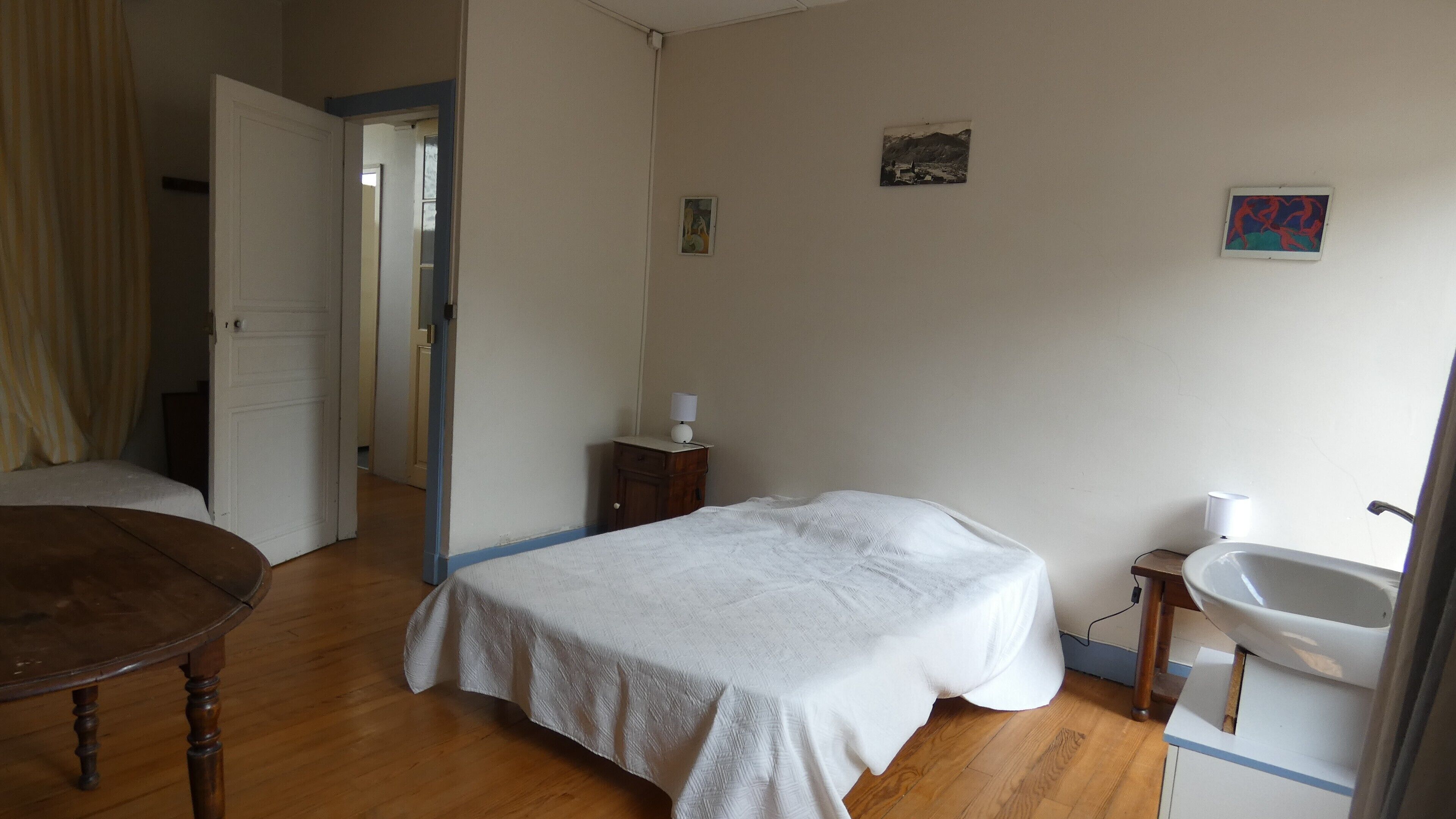 A bedroom with a bed, bedside table, lamp, and a bathroom with a sink and mirror.