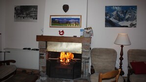 Ein Wohnzimmer mit Kamin, Heizkörper, einem gerahmten Bild von einem Gebirge und zwei Sesseln.
