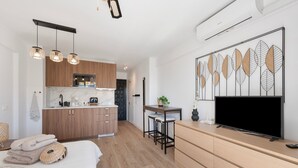 Moderni hotellihuone, jossa on sänky, televisio, työpöytä tuolilla, keittiöalue ja koristeellinen seinäelementti.