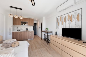 A modern hotel room with a bed, a TV, a desk with a chair, a kitchen area, and a decorative wall piece. - Boho Studio Apartment with Balcony, Wi-Fi and Air Conditioning (Marbella)