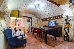 A rustic room with a stone wall, a wooden table, a sofa, a TV, and a statue. - La Casa di Simone - Palazzolo Acreide (Palazzolo Acreide)