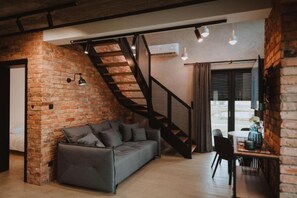 A modern living space with a brick wall, a grey sofa, a staircase, and a dining area with a table and chairs. - Large Holiday Home With a Jacuzzi on the Terrace (Koscierzyna)