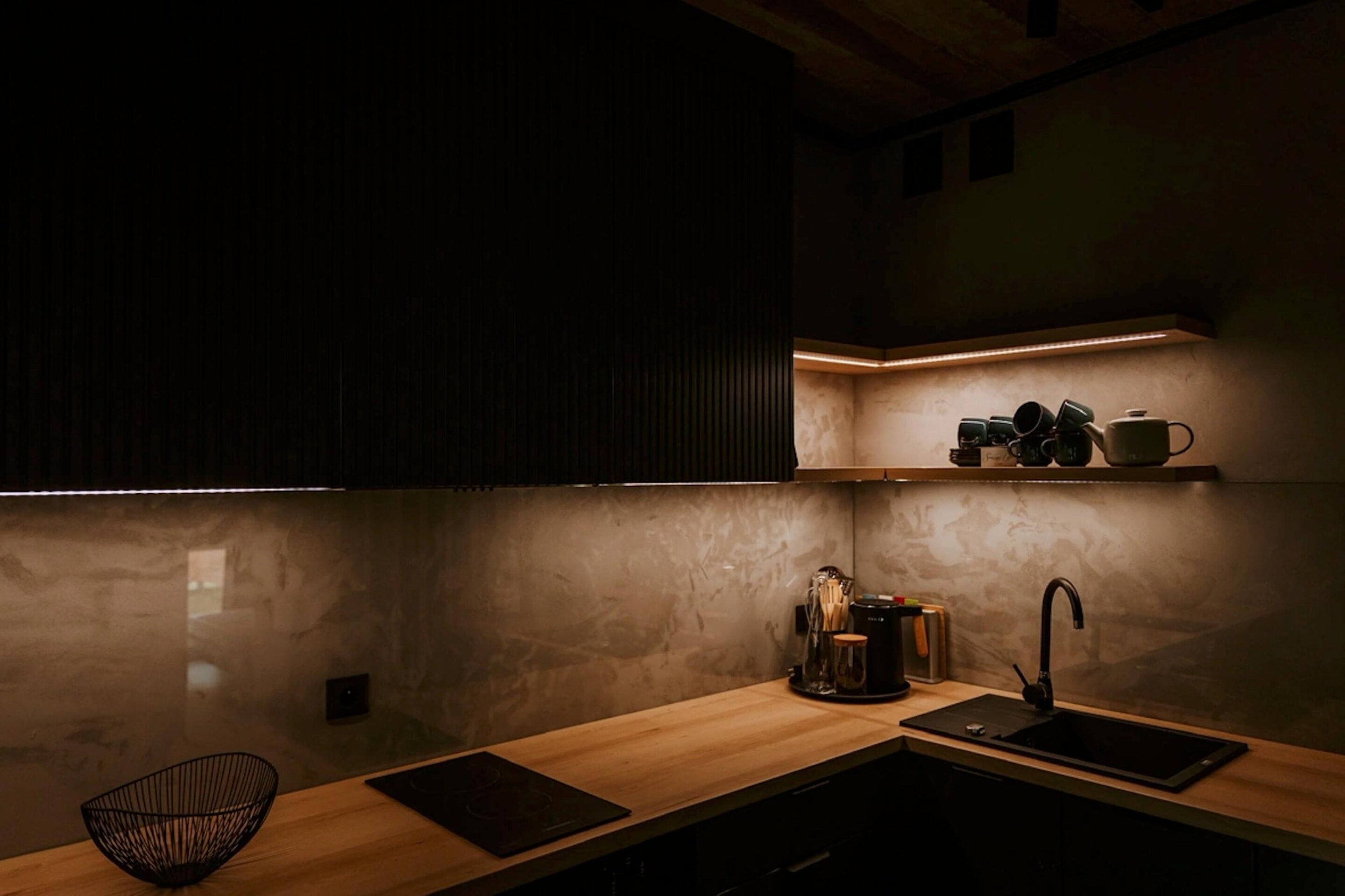 A modern kitchen with a wooden countertop, a black induction cooktop, a sink, and a black wire basket.