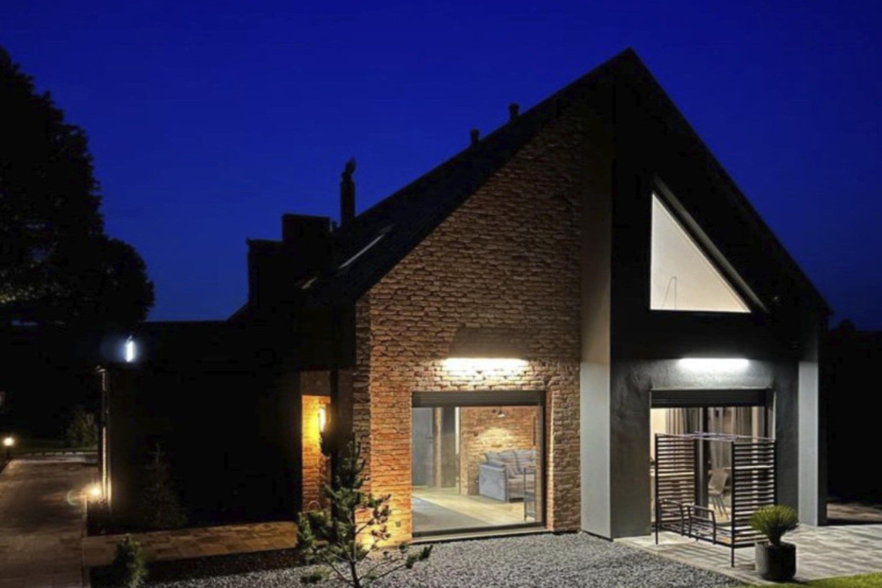 A modern house with a sloped roof, a large glass door entrance, and a well-lit interior.