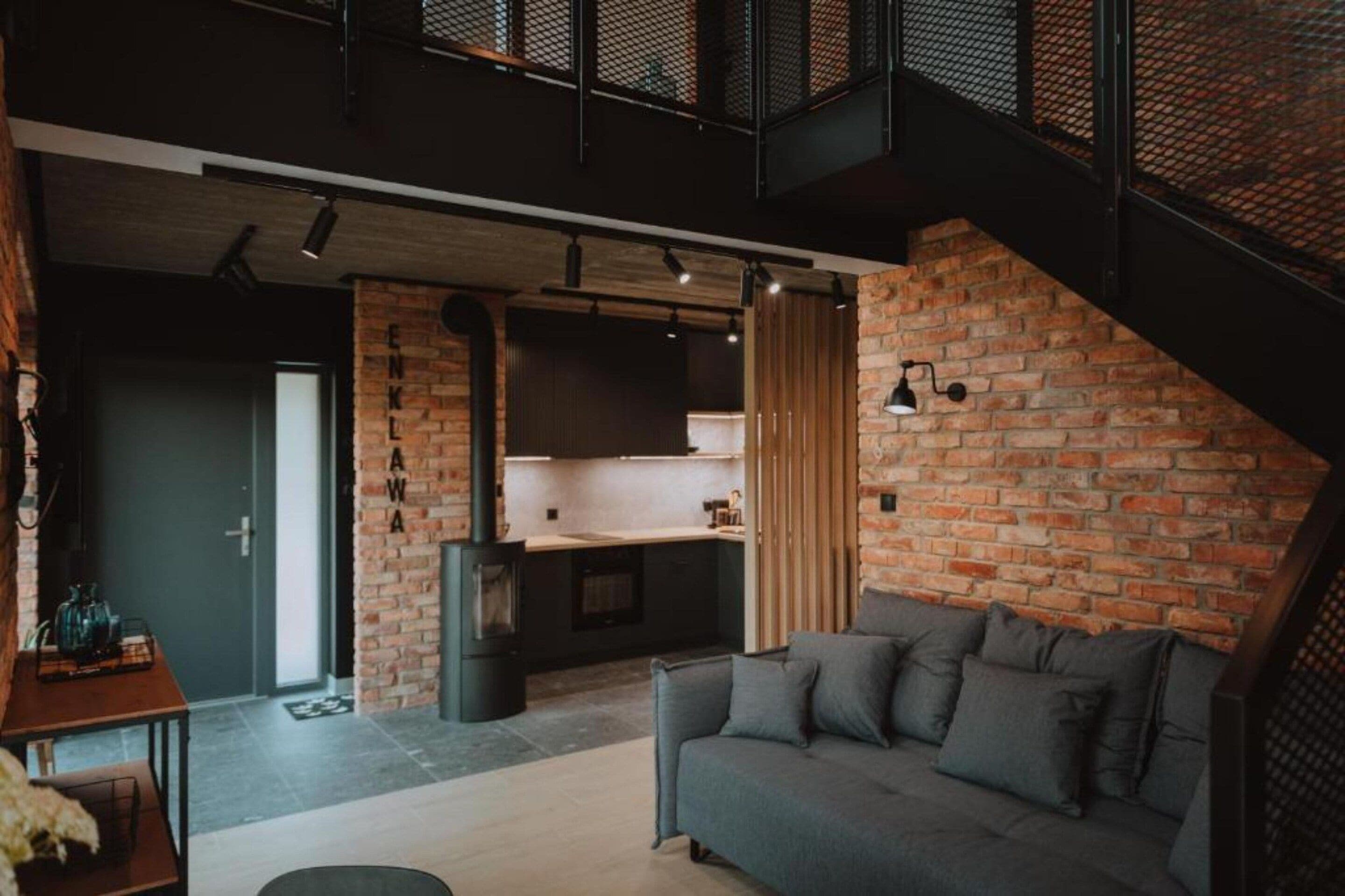 A modern interior with a brick wall, a sofa, a kitchen area, and a staircase.