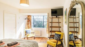 Ein Schlafzimmer mit Bett, Sessel, Fernseher, Fenster und Spiegel.