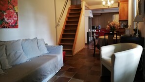 A living room with a sofa, a chair, a staircase, and a kitchen area in the background. - LE GITE DU CHATEAU NEAR MARAIS POITEVIN (Fors)