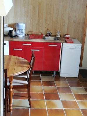 Eine kleine Küche mit roten Schränken, einem weißen Geschirrspüler und einem Holzespeisetisch.