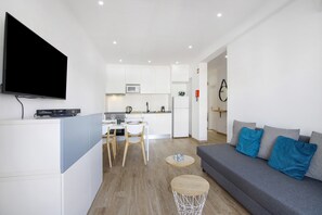Un espacio habitable moderno con un televisor de pantalla plana, un comedor, una cocina y un sofá gris con cojines azules.