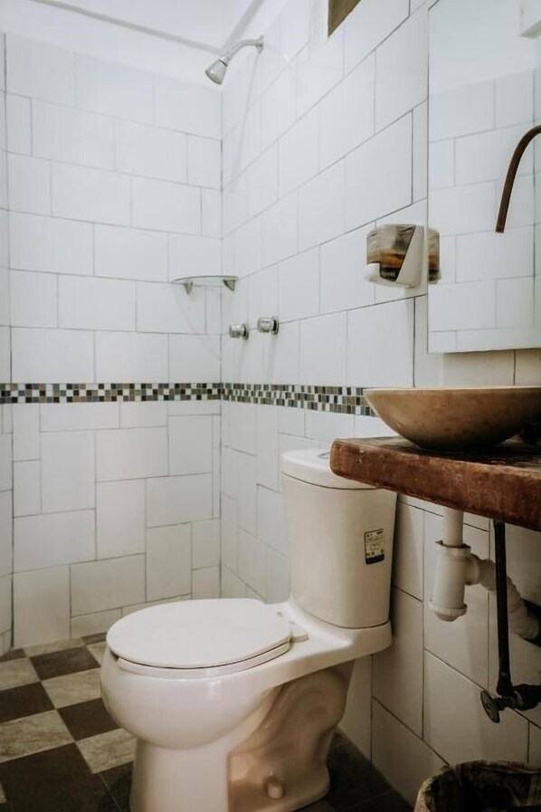 Une salle de bain avec des carreaux blancs, un sol à carreaux, des toilettes, un lavabo en bois et une douche.