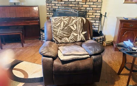 A leather armchair with a patterned throw, a fireplace, a wooden desk, and a small table with a laptop.