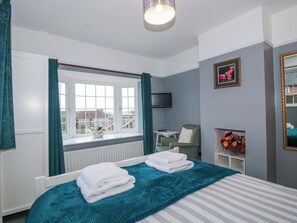 A bedroom with a bed, a window with curtains, a chair, a TV, and a framed picture on the wall. - The Rumbles (Ludlow)