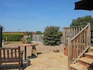 A patio area with a wooden table and chairs, a stone bench, a wooden fence, and a staircase leading to a brick structure. - The Rumbles (Ludlow)
