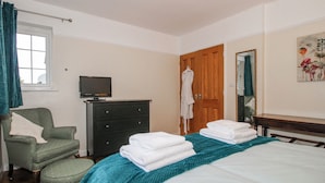 Un dormitorio con cama, una silla, cómoda, televisor y puerta.