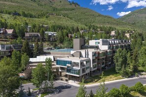 Ein modernes Hotel mit mehreren Etagen, einem Schwimmbad und einer Bergkulisse.