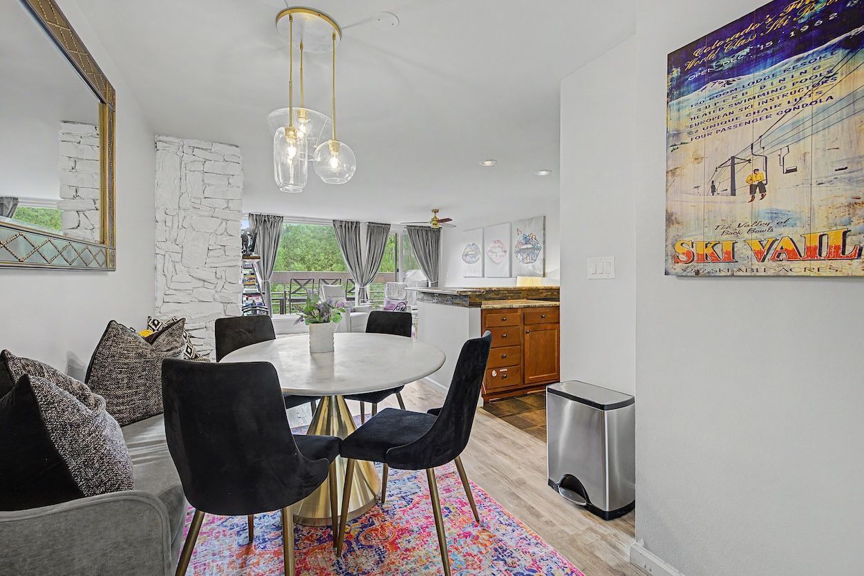 A modern dining area with a round table, black chairs, and a colorful rug.