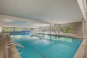 Ein Innenpool mit großen Glaswänden, Fliesenboden und Decke mit geometrischem Muster.