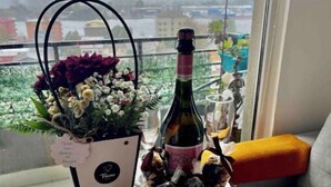 A small wooden table with a bottle of wine, a bouquet of flowers, and a decorative item. - River view Downtown apartment 12th floor (Valdivia)