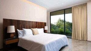 Una habitación de hotel moderna con una cama grande, cabecera de madera, dos lámparas de noche y un amplio ventanal con cortinas.