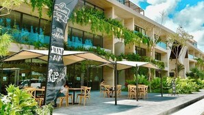 Un edificio moderno con mesas al aire libre, una bandera con el texto 'Mercadito Mini Market' y abundante vegetación.