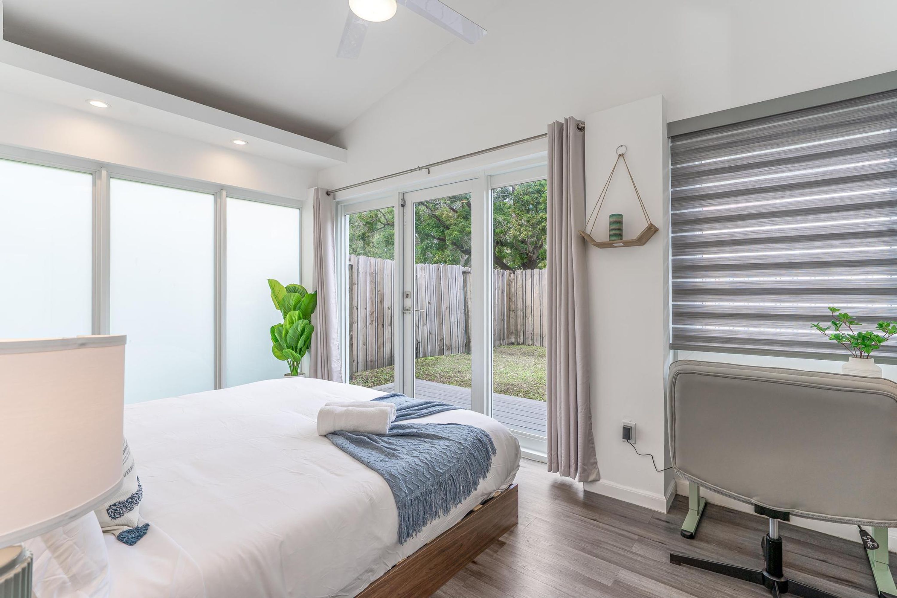 A bedroom with a bed, a desk, a chair, a window, and a view of the outdoors.