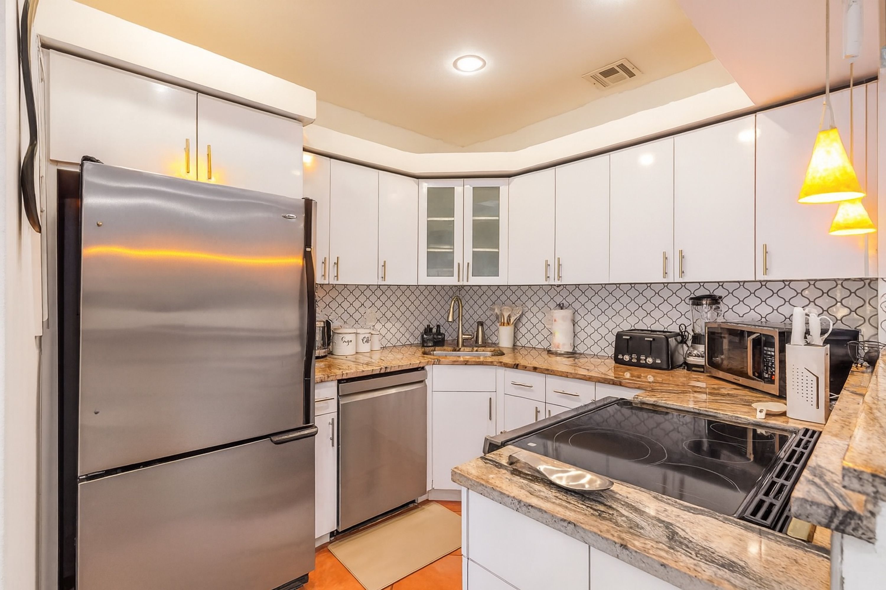 Cocina moderna con electrodomésticos de acero inoxidable, armarios blancos, encimera negra y salpicadero con diseño.