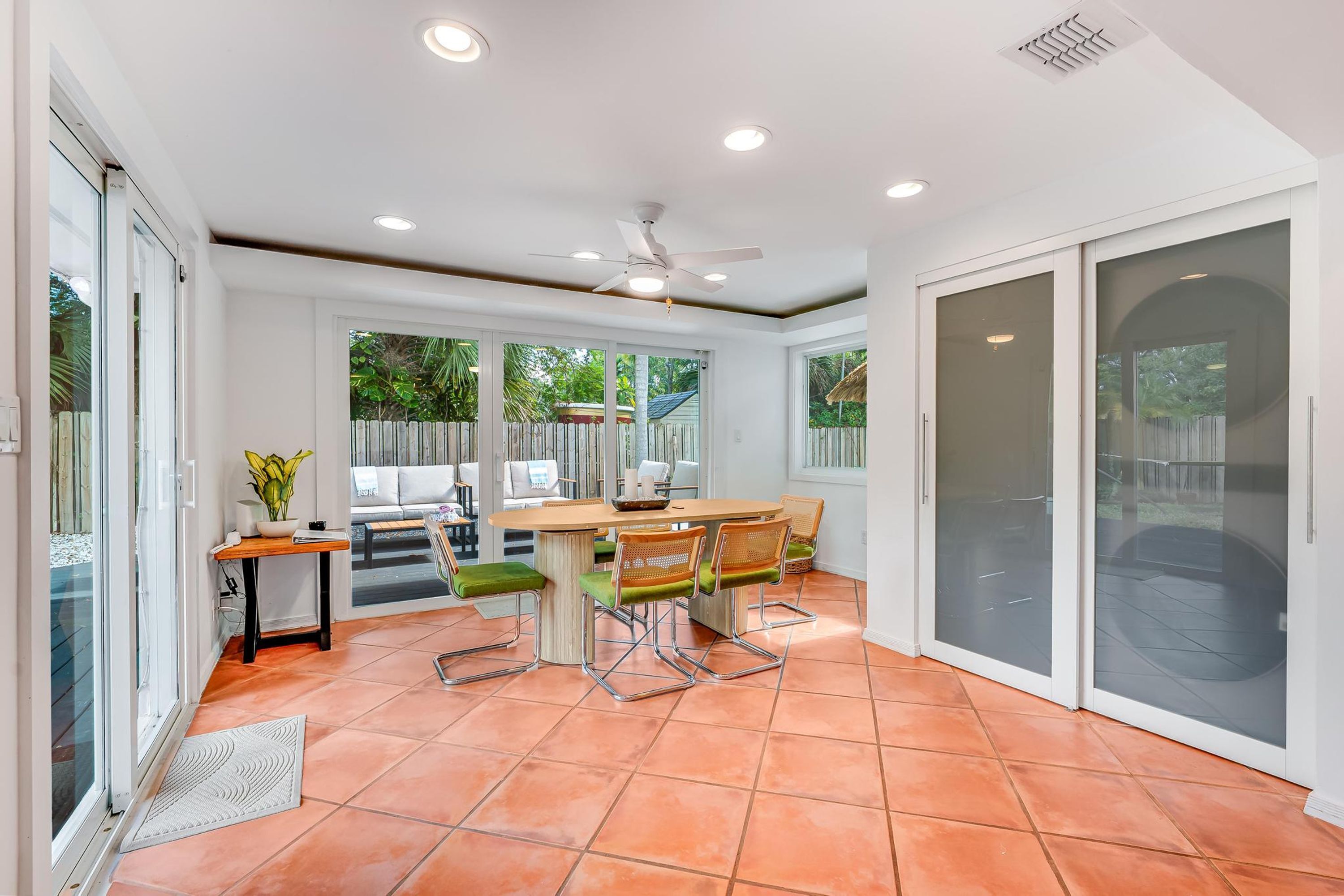 A dining area with a round table, four chairs, a ceiling fan, and large sliding glass doors.