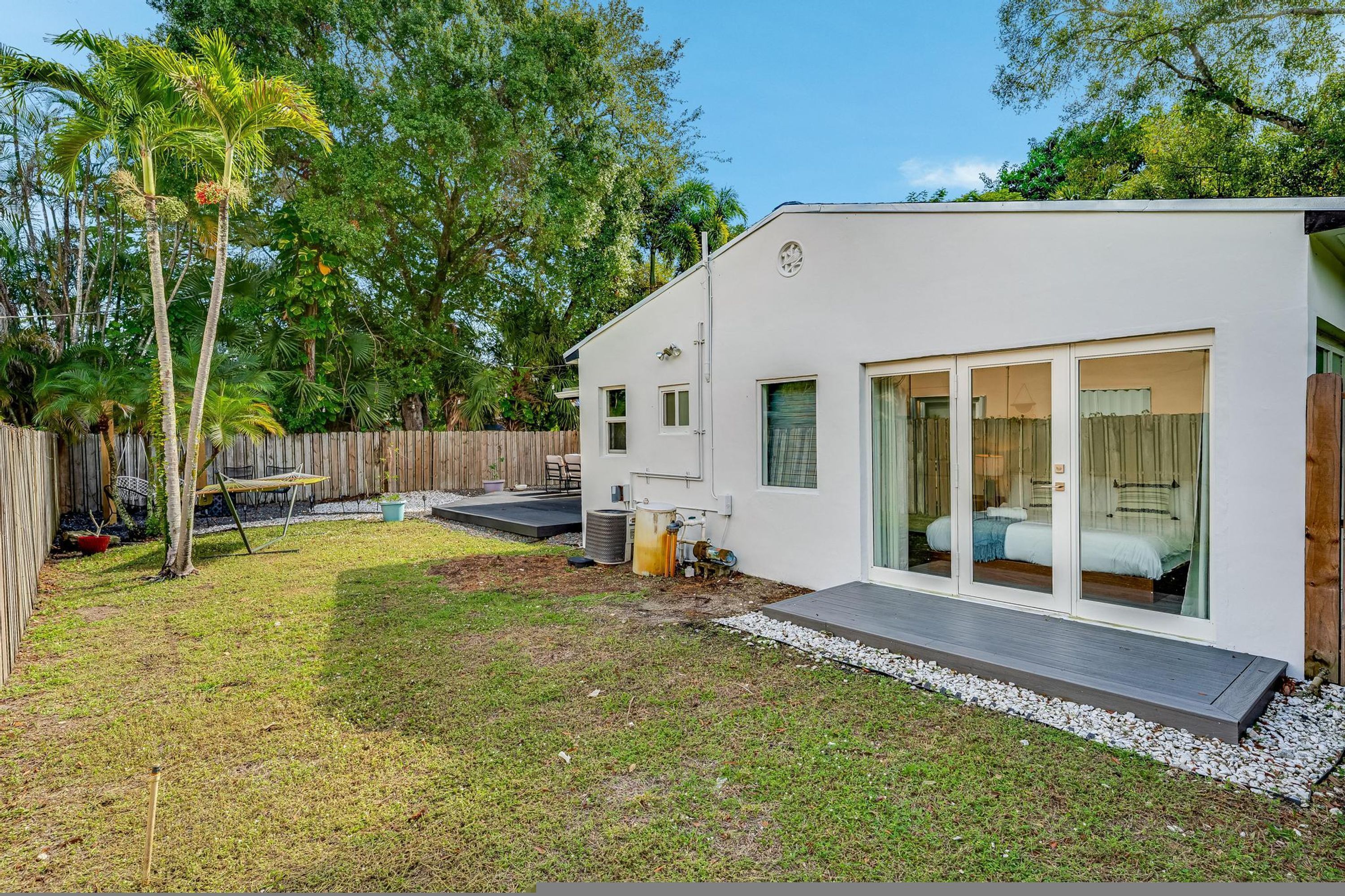 A modern house with a large glass door leading to a bedroom, a small patio, and a wooden fence.