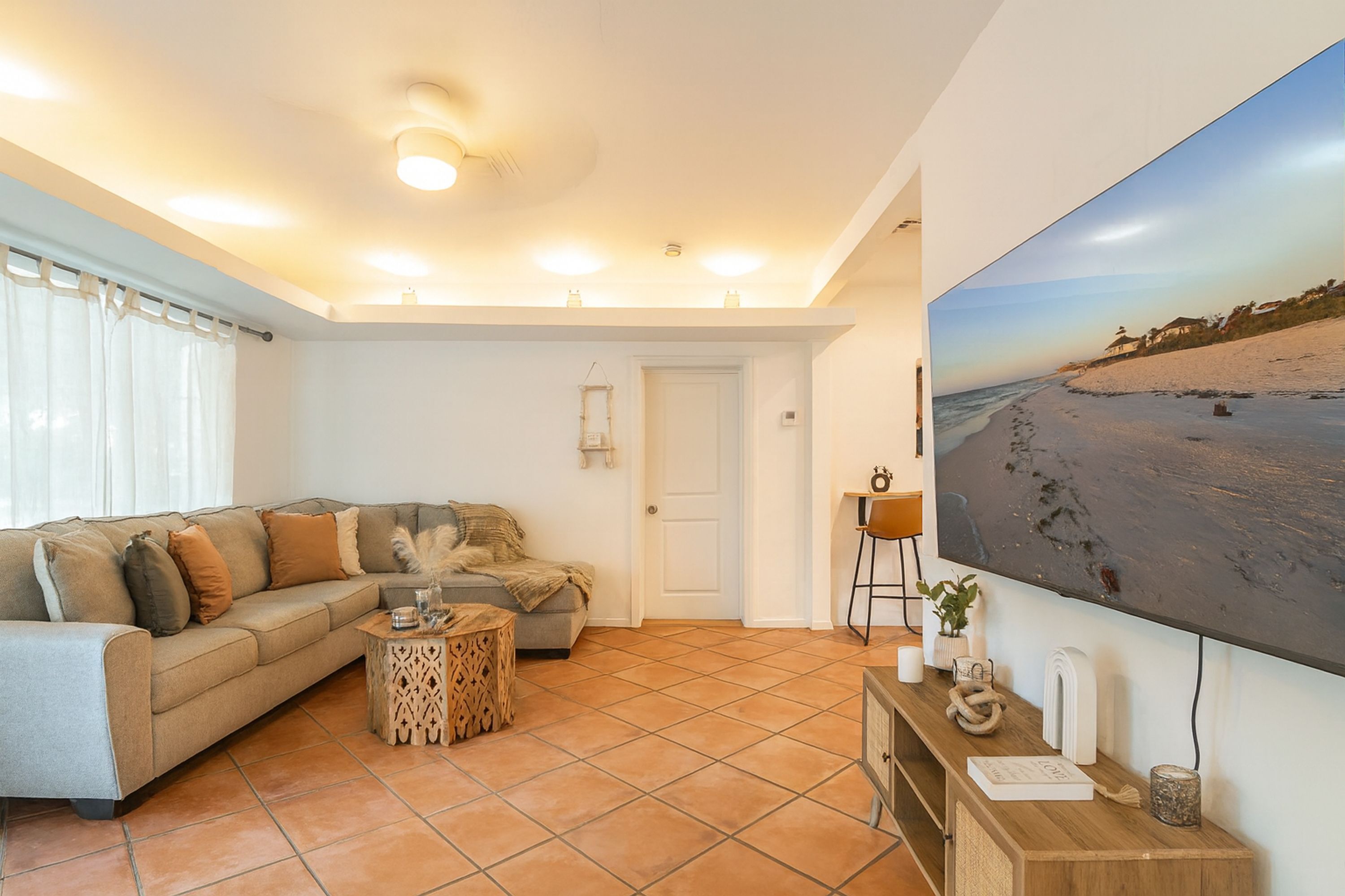 Una sala de estar con un sofá, una mesa de centro, un televisor y un cuadro de una playa.