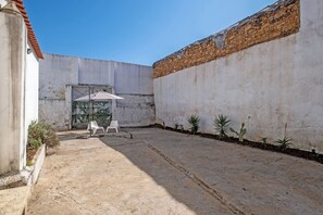 Ein Innenhof mit Betonboden, einem weißen Plastikstuhl, einem kleinen Tisch und einem Blumentopf.