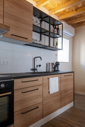 Eine moderne Küche mit Holzschränken, einer schwarzen Arbeitsplatte, einem integrierten Weinkühlschrank und einem Fenster.