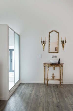 Ein Badezimmer mit einem großen Fenster, einem weißen Waschbecken, einem spiegel mit goldener Rahmung und Wandleuchten.