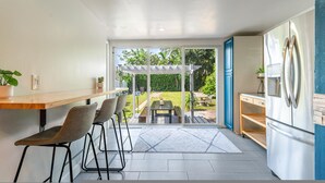 A modern kitchen with a large refrigerator, bar stools, a dining table, and a view of a backyard with a pergola. - The Reef in Fort Lauderdale (Fort Lauderdale)