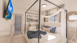 Une chambre à coucher avec un lit à baldaquin, un téléviseur à écran plat, un tableau, une table de chevet et une lampe.