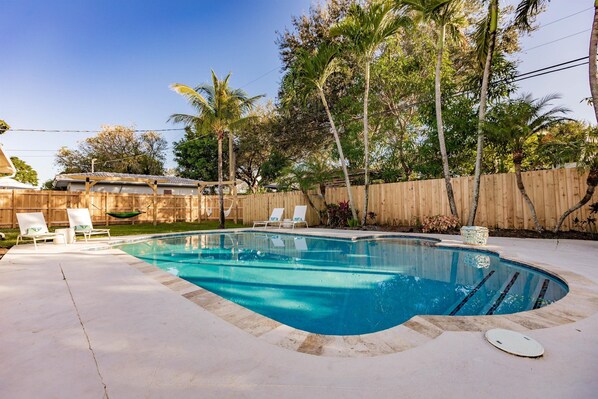 Ein rechteckiger Pool mit Holzzaun und Palmen im Hintergrund.