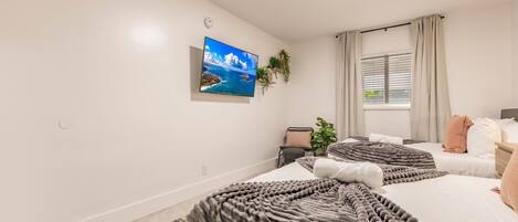 Un dormitorio con dos camas, un televisor en la pared, una ventana con cortinas y una planta.