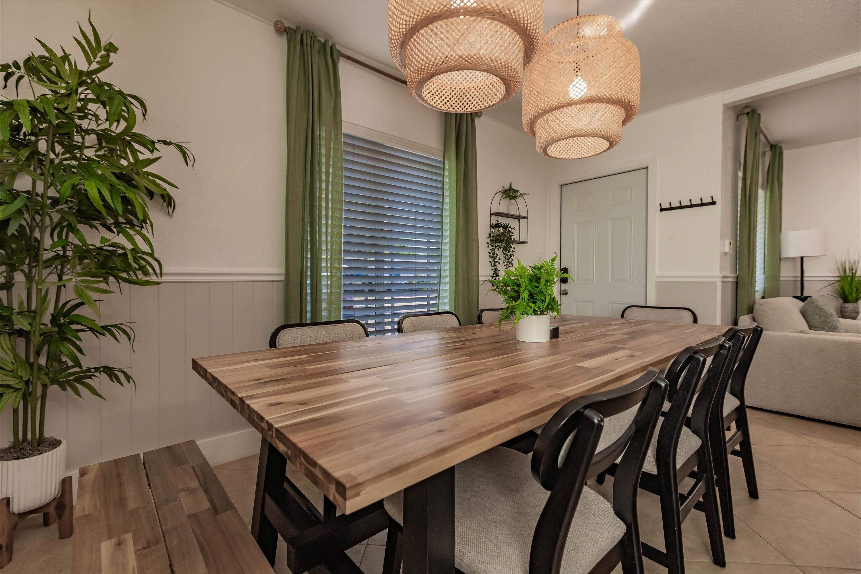 Un coin repas avec une table en bois, des chaises, des rideaux verts et des lampes en rotin suspendues.