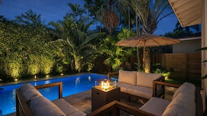 A poolside area with a seating arrangement, a fire pit, and surrounding tropical vegetation. - Fox Pearl 4Bd Pool House- Las Olas Luxury Getaway (Fort Lauderdale)