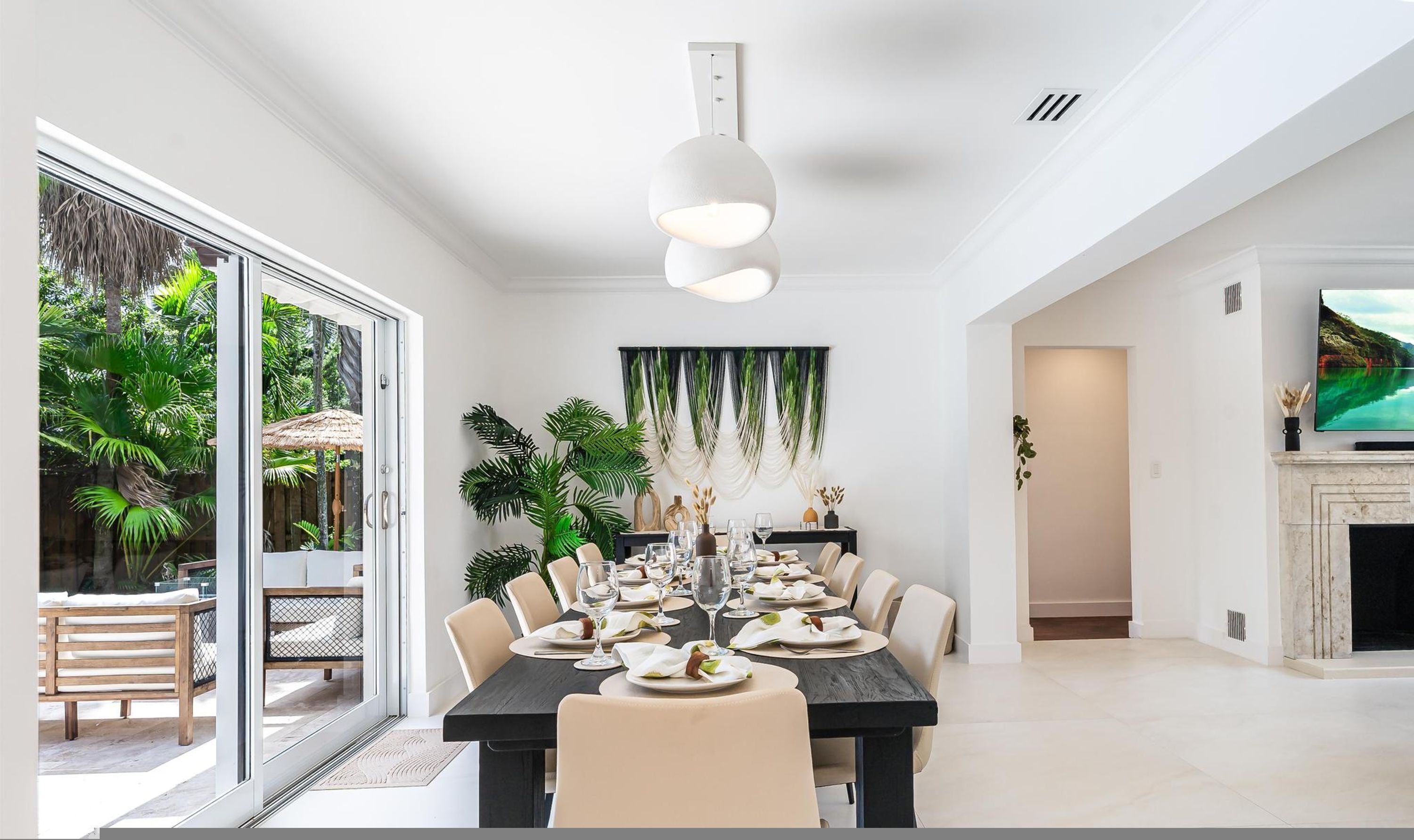 Comedor con una mesa larga, sillas, una lámpara moderna y un televisor montado en la pared.