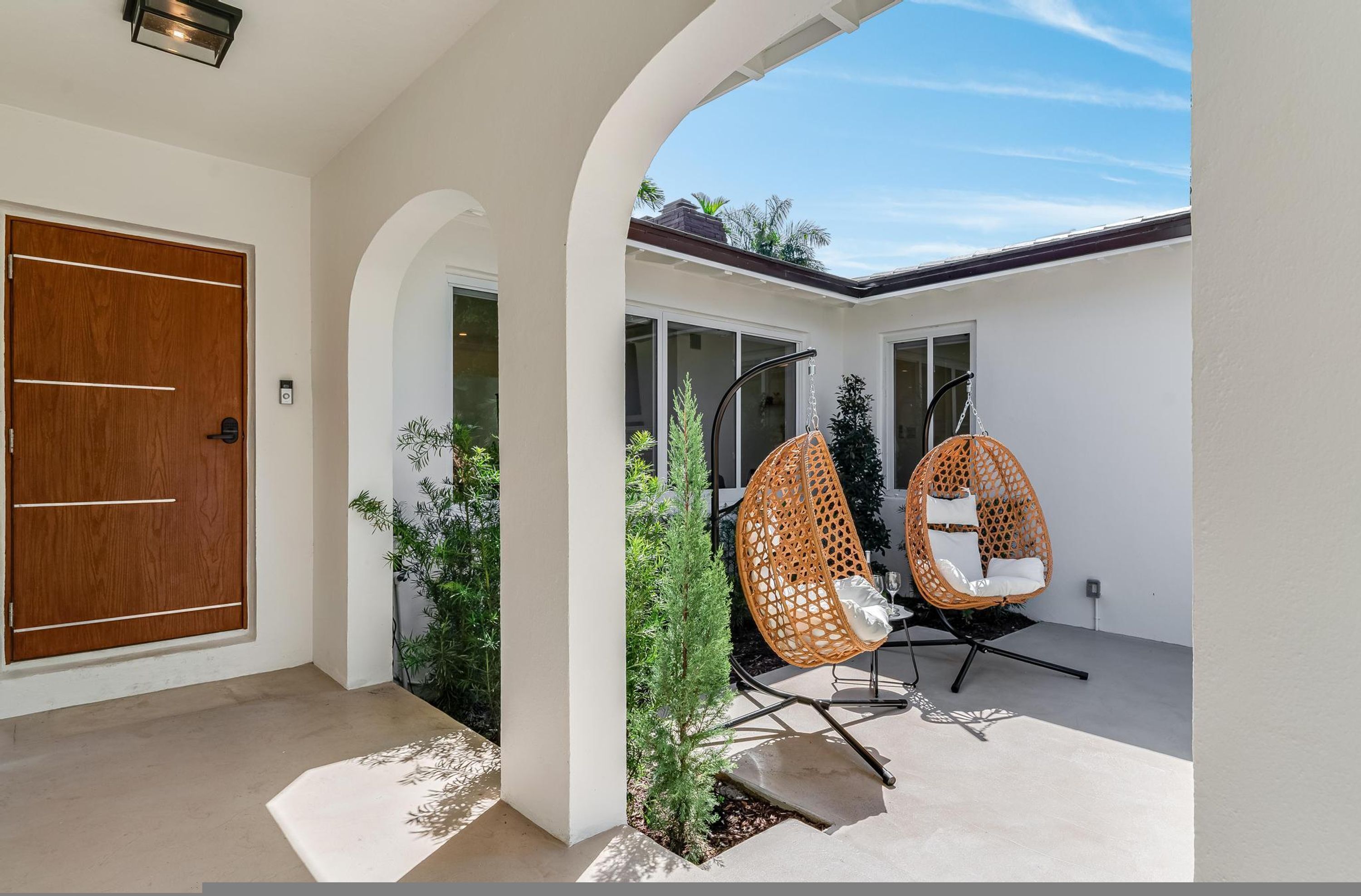 Una casa moderna con puerta de madera, dos sillones de mimbre y un pequeño jardín.