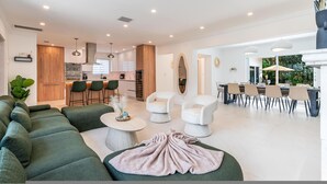 A modern living room with a sectional sofa, a round coffee table, and a dining area with a long table and chairs. - Fox Pearl 4Bd Pool House- Las Olas Luxury Getaway (Fort Lauderdale)