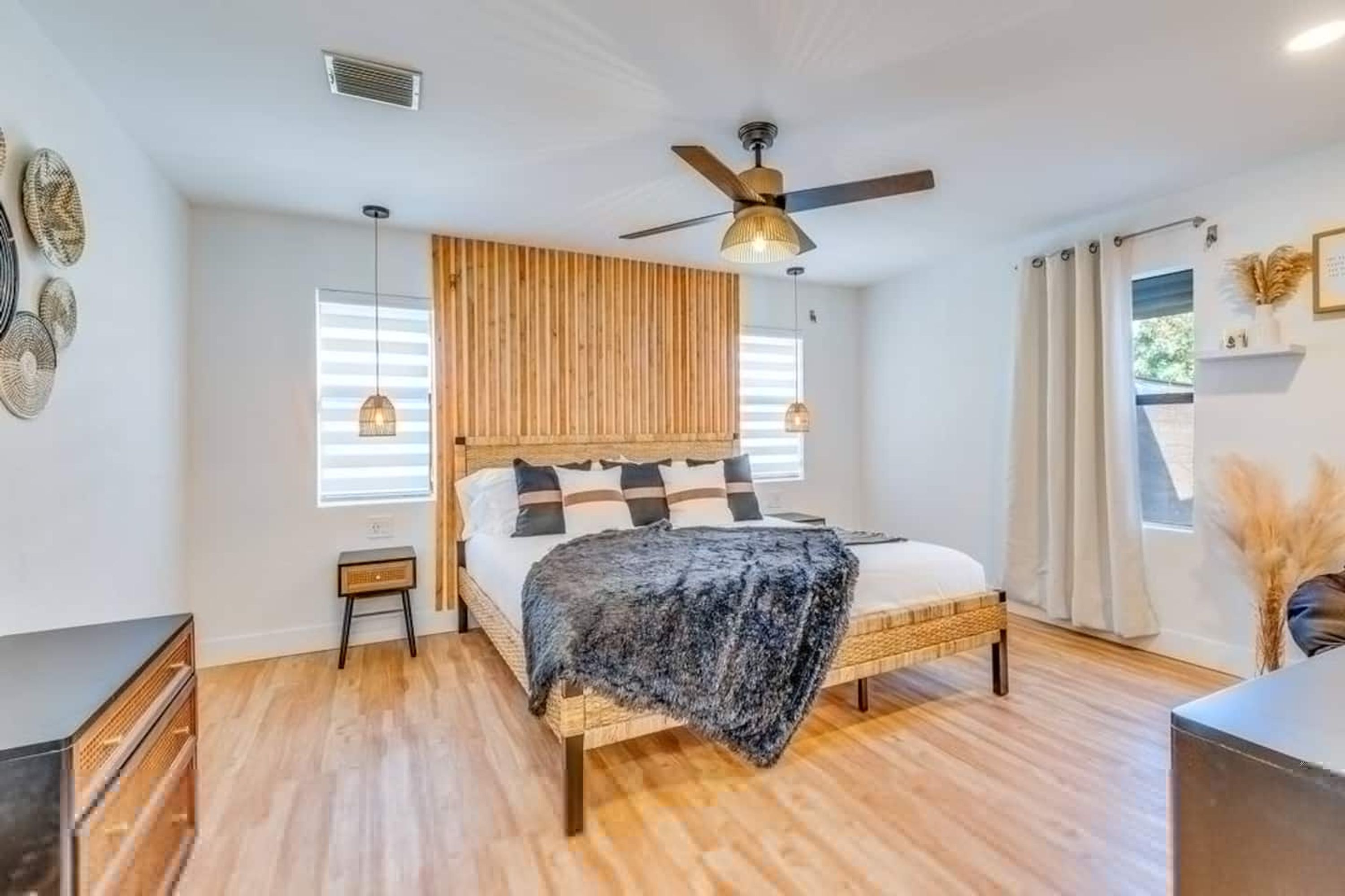 Un dormitorio con cama, cabecero de madera, ventilador de techo, lámparas de noche y una ventana con persianas.