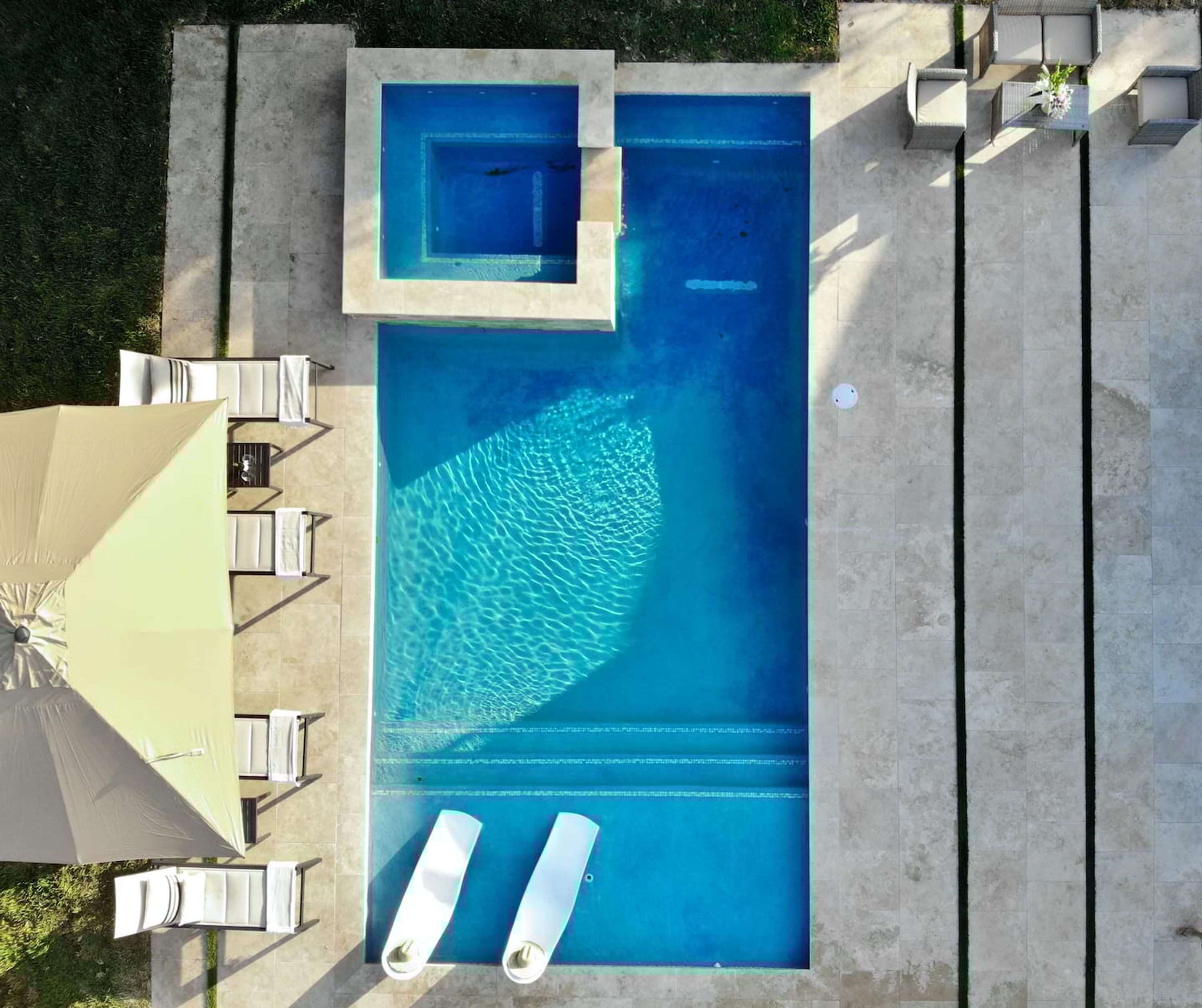 A rectangular swimming pool with a small hot tub, surrounded by a concrete deck and outdoor seating.