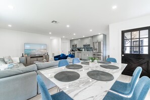 Un salon moderne avec une table en marbre, des chaises bleues, un canapé gris et une cuisine en arrière-plan.