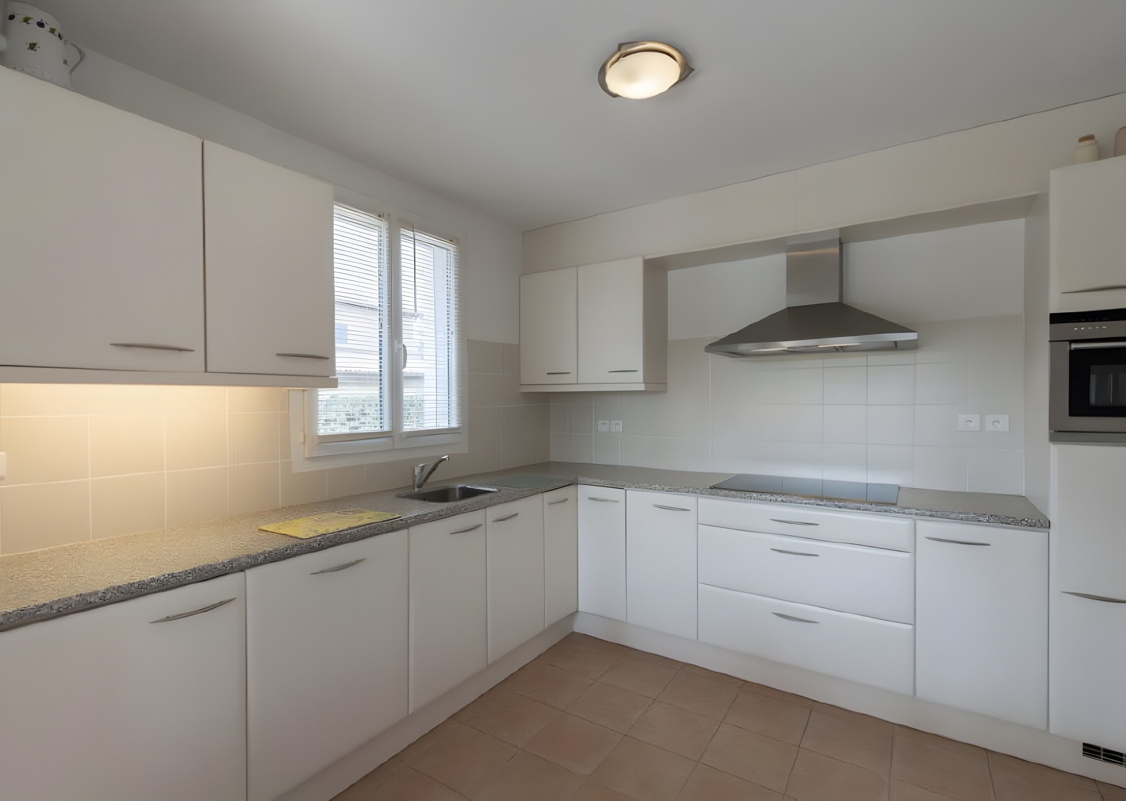 A modern kitchen with white cabinets, a stainless steel range hood, and a window with blinds.