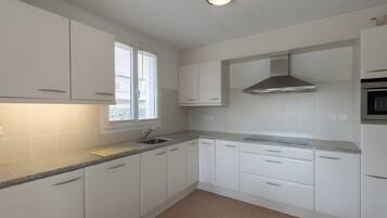 A modern kitchen with white cabinets, a stainless steel range hood, and a window with blinds.