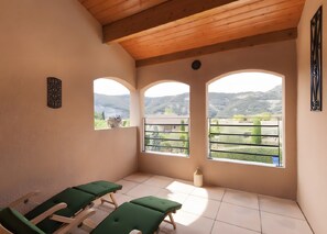 A room with three green reclining chairs, a tiled floor, and a view of a mountainous landscape through arched windows. - Ardèche Villa for Rent (Vallon-Pont-d'Arc)